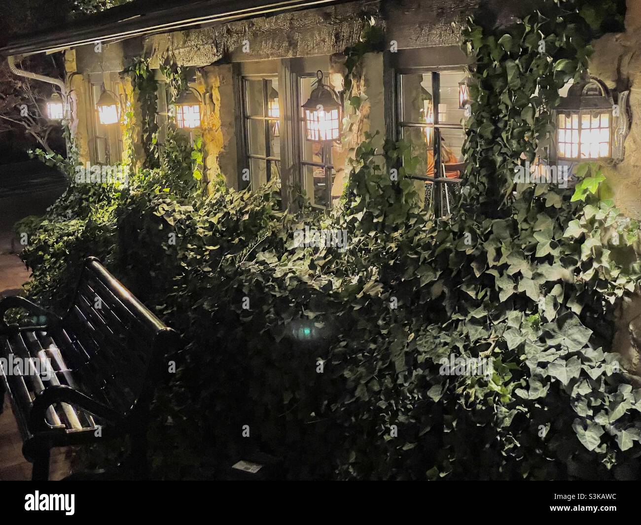 An ivy covered storefront is illuminated at dusk at Gardner Village in Utah, USA during its’ annual “WitchFest” each October. You can see shoppers and patrons milling about through the shop windows, - Smartphone Captured Stock Image