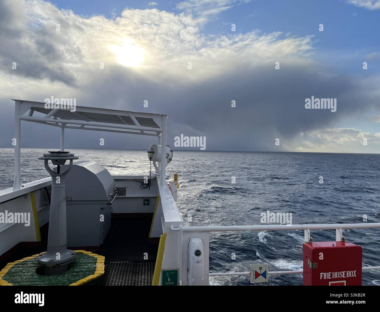 Wing of the navigational bridge with gyro compass repeater, remote control for manoeuvring and Panama shelter. In background is huge rainy cloud cumulonimbus with snow precipitation. Stock Photo