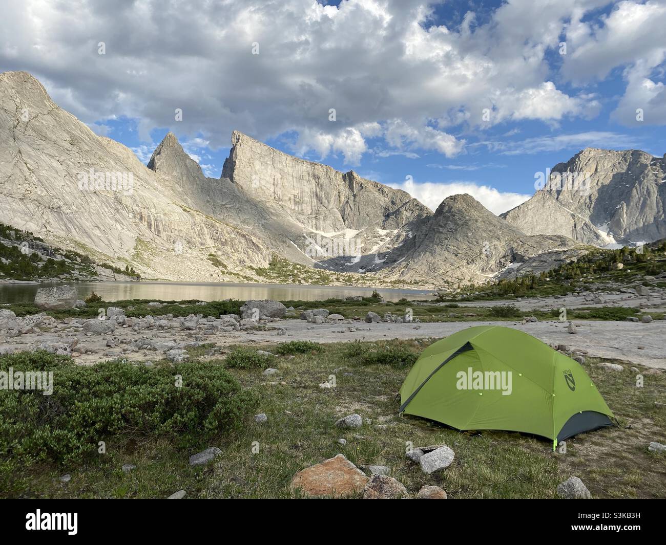 Backcountry campsite with tent in foreground overlooking deep lake and east temple peak on a sunny summer day in Bridger-Teton National Forest, Wyoming, USA - Smartphone Captured Stock Image