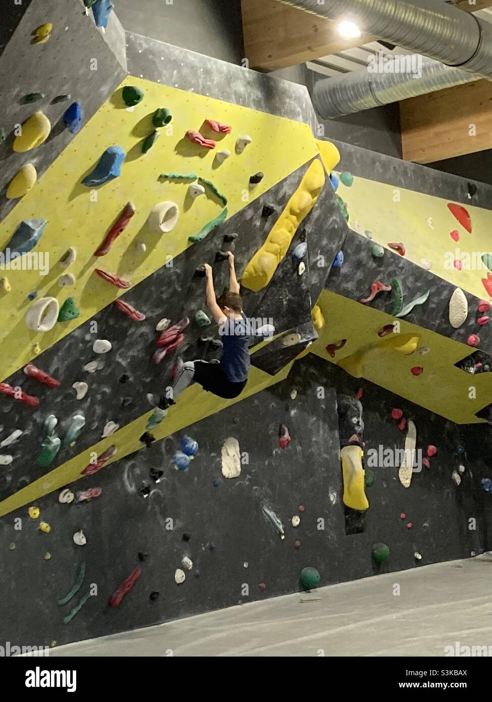 A Teenager climbs in an indoor bouldering hall - Smartphone Captured Stock Image