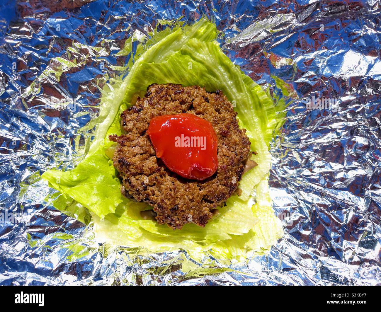 Ground beef hamburger with ketchup and lettuce leaf on foil , fancy fast food gluten free dairy fee Keto - Smartphone Captured Stock Image