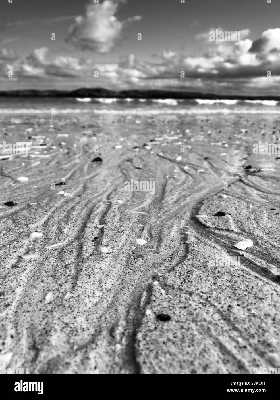 Close up view of the sand on a beach with the sea behind in black and white Stock Photo