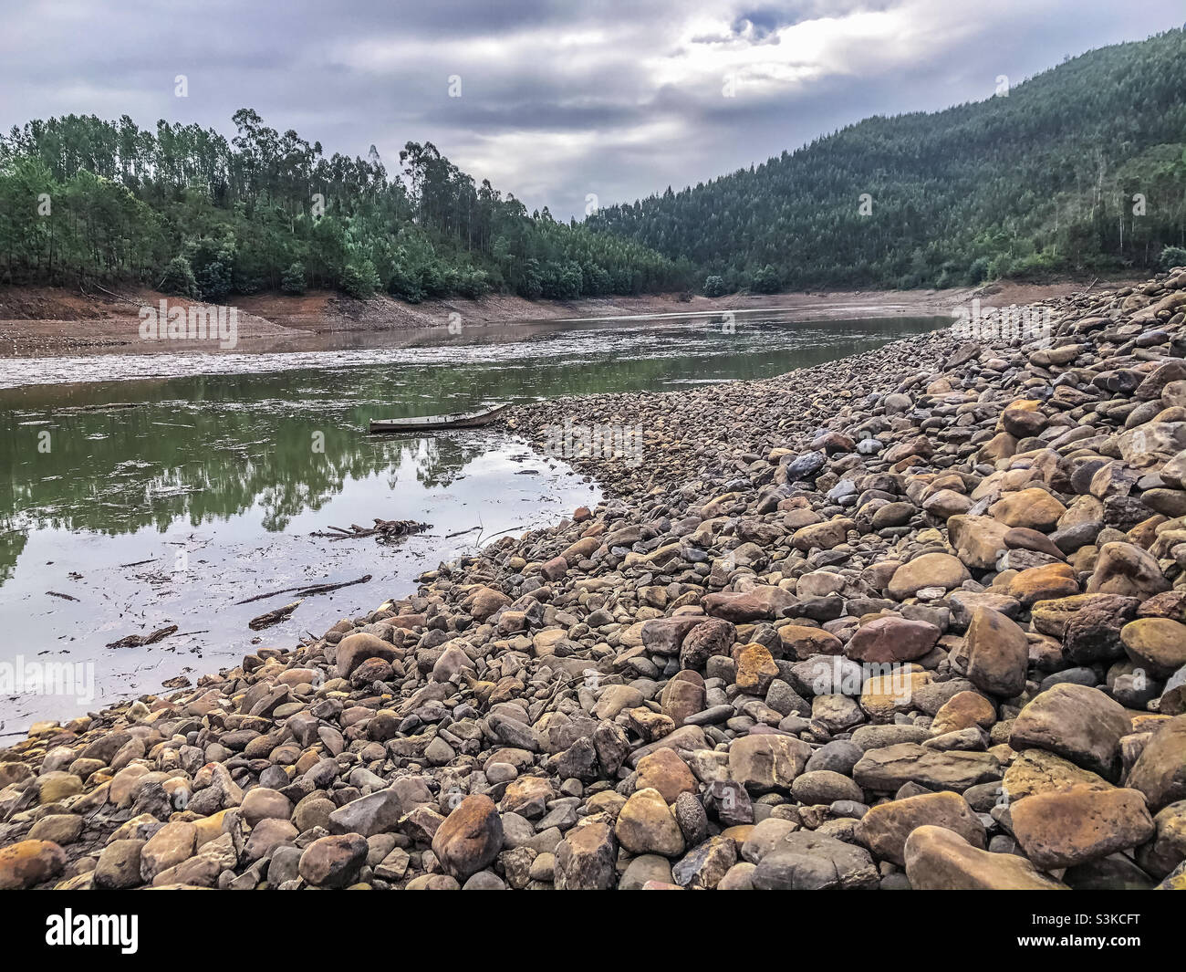Autumnal scene of a stony river beach and water surrounded by tree covered hills - Smartphone Captured Stock Image