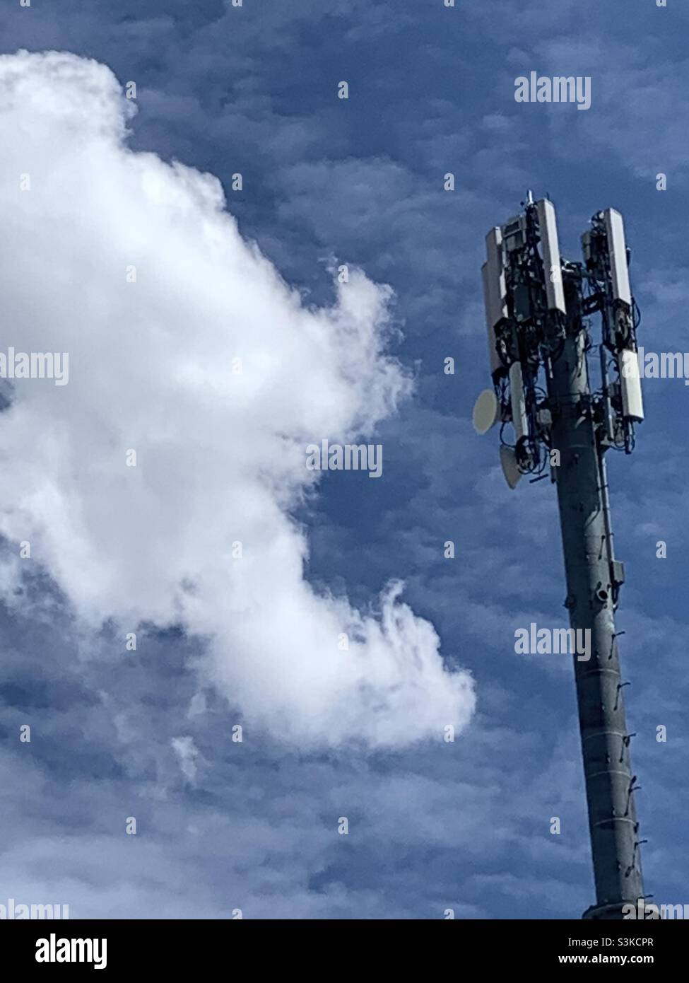 A cell tower set against an early springtime blue sky and billowing clouds. - Smartphone Captured Stock Image