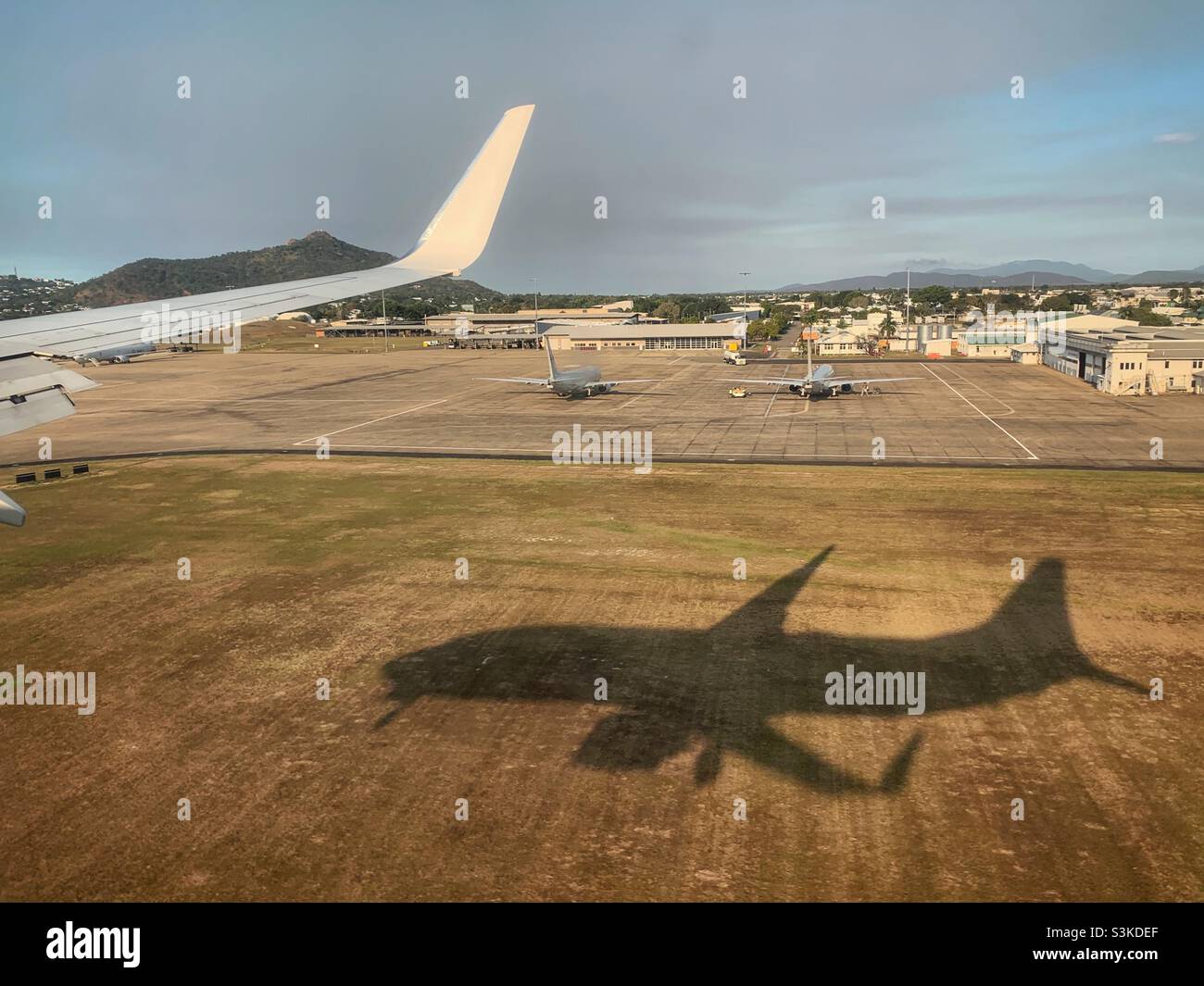 The shadow of a Boeing 737-800 landing at Townsville Airport, Queensland, Australia showing the wing tip and military aircraft in the background. Stock Photo