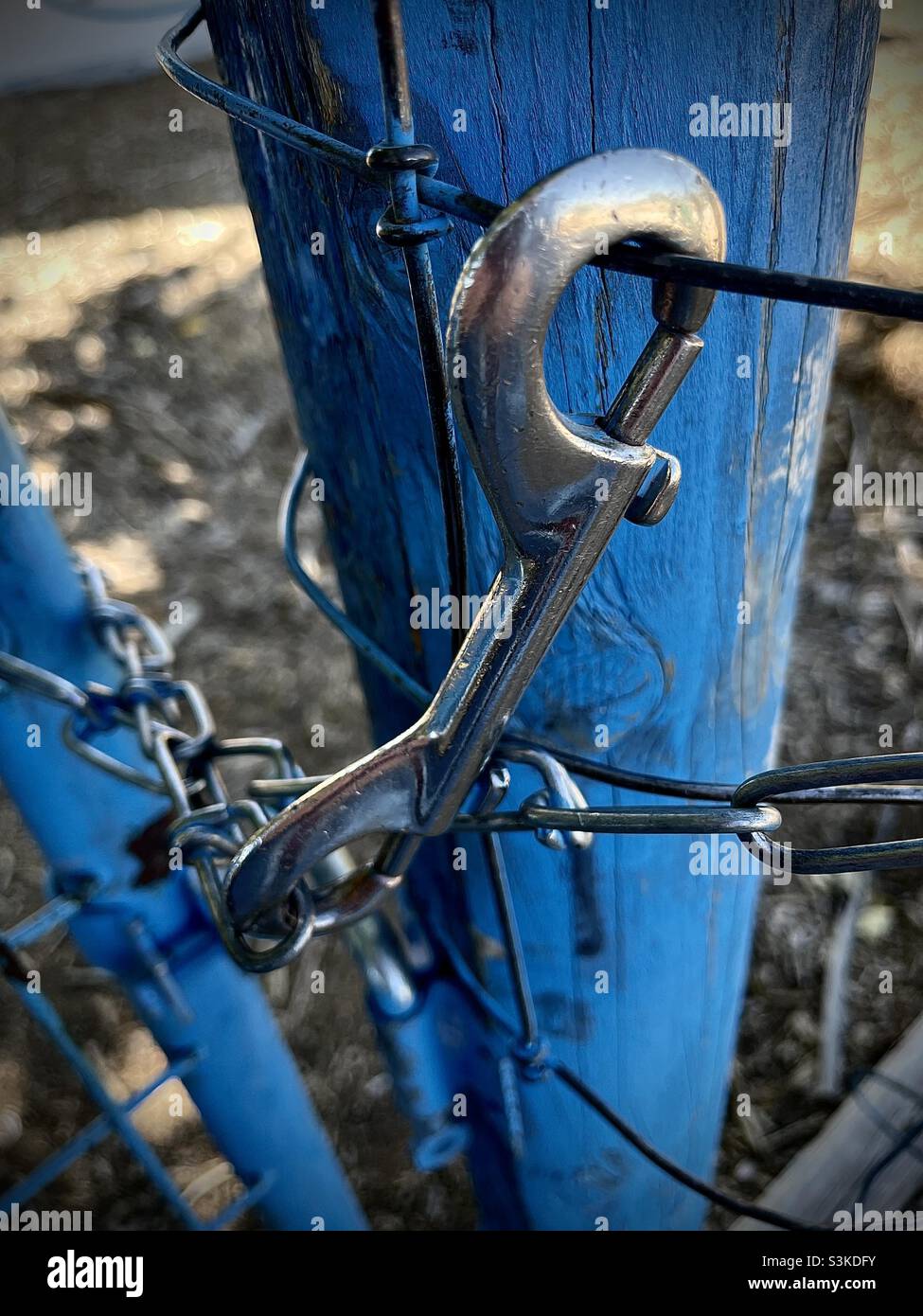 Up close image of a double end snap hook clip securing a blue gate closed  with chain and wire to a blue post Stock Photo - Alamy