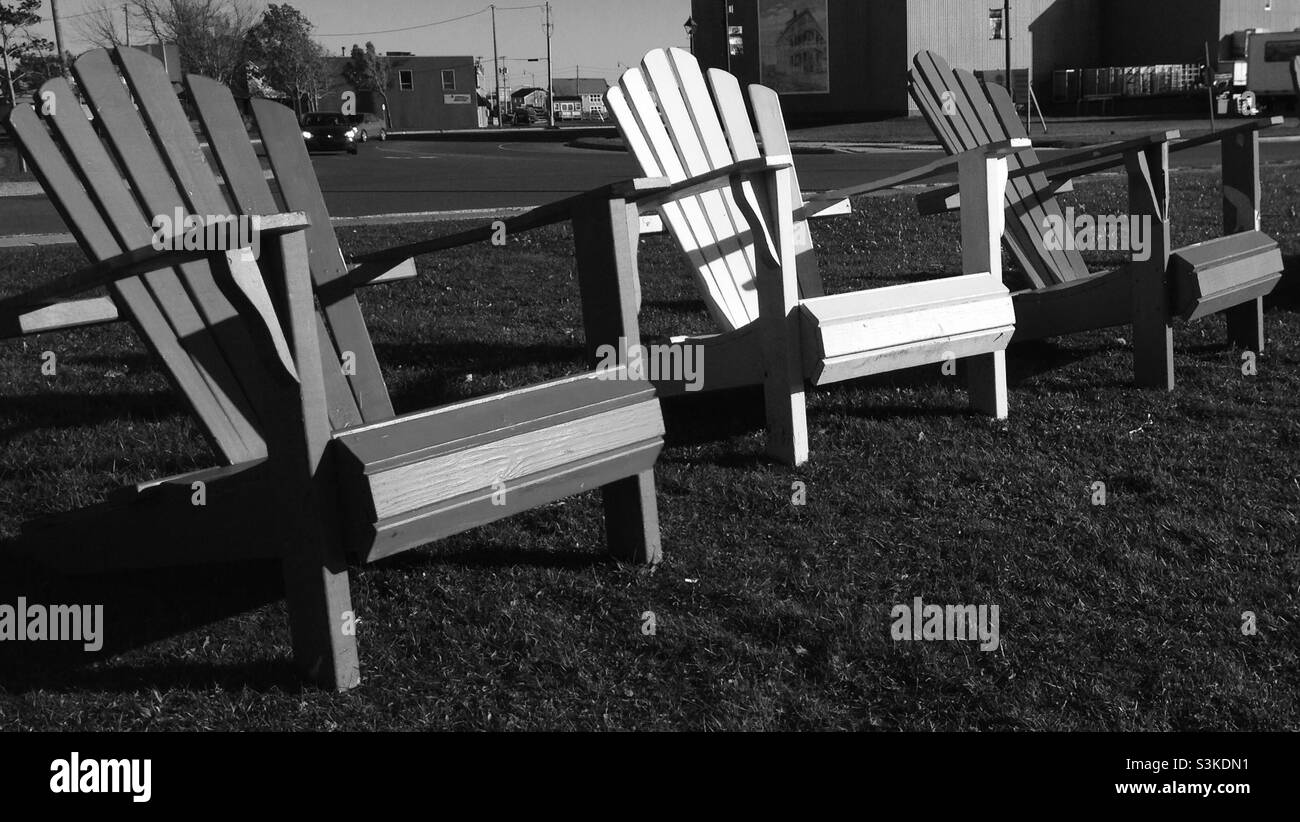 Adirondack chairs in a small park facing the harbour,water, a place to rest for a while Black and white photo Stock Photo