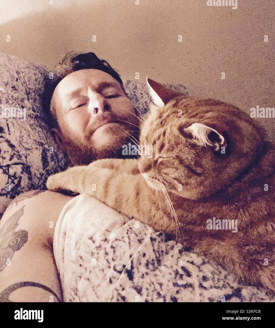 A cat lies on a mans chest while he is sleeping in bed - Smartphone Captured Stock Image