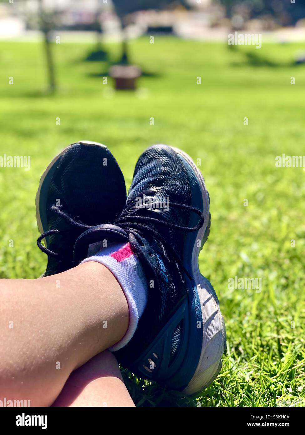 Crossed feet wearing tennis shoes or sneakers in green grass lit by bright sunlight. Stock Photo