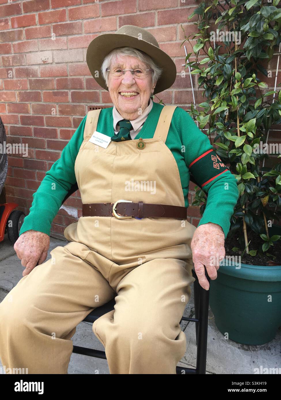 90 year old women’s land army veteran relaxing in her garden in uniform. Portrait of Annie Duplock Stock Photo