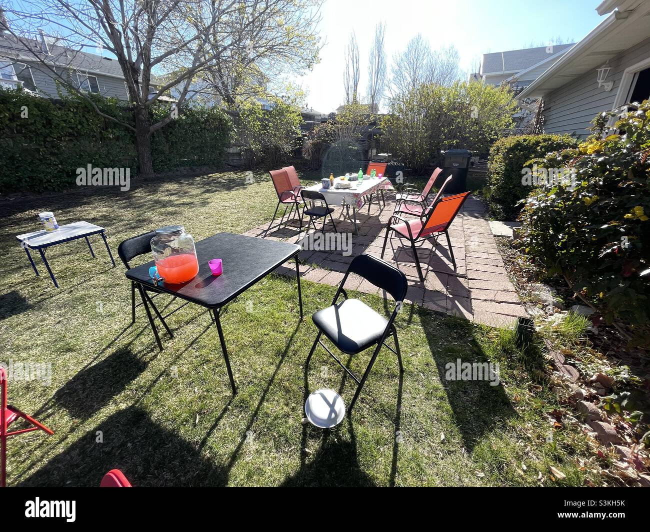 A patio and backyard in the summertime after a family get together and party. Cleanup is still incomplete with tables, chairs, food and drink leftovers lying about. Stock Photo