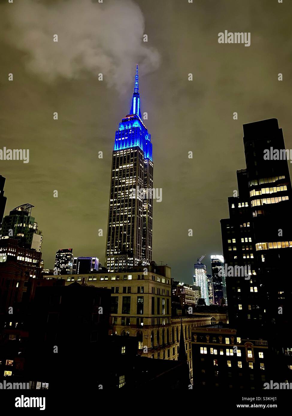 Bright blue lights on top of the Empire State building against a grey cloudy sky in New York City - Smartphone Captured Stock Image