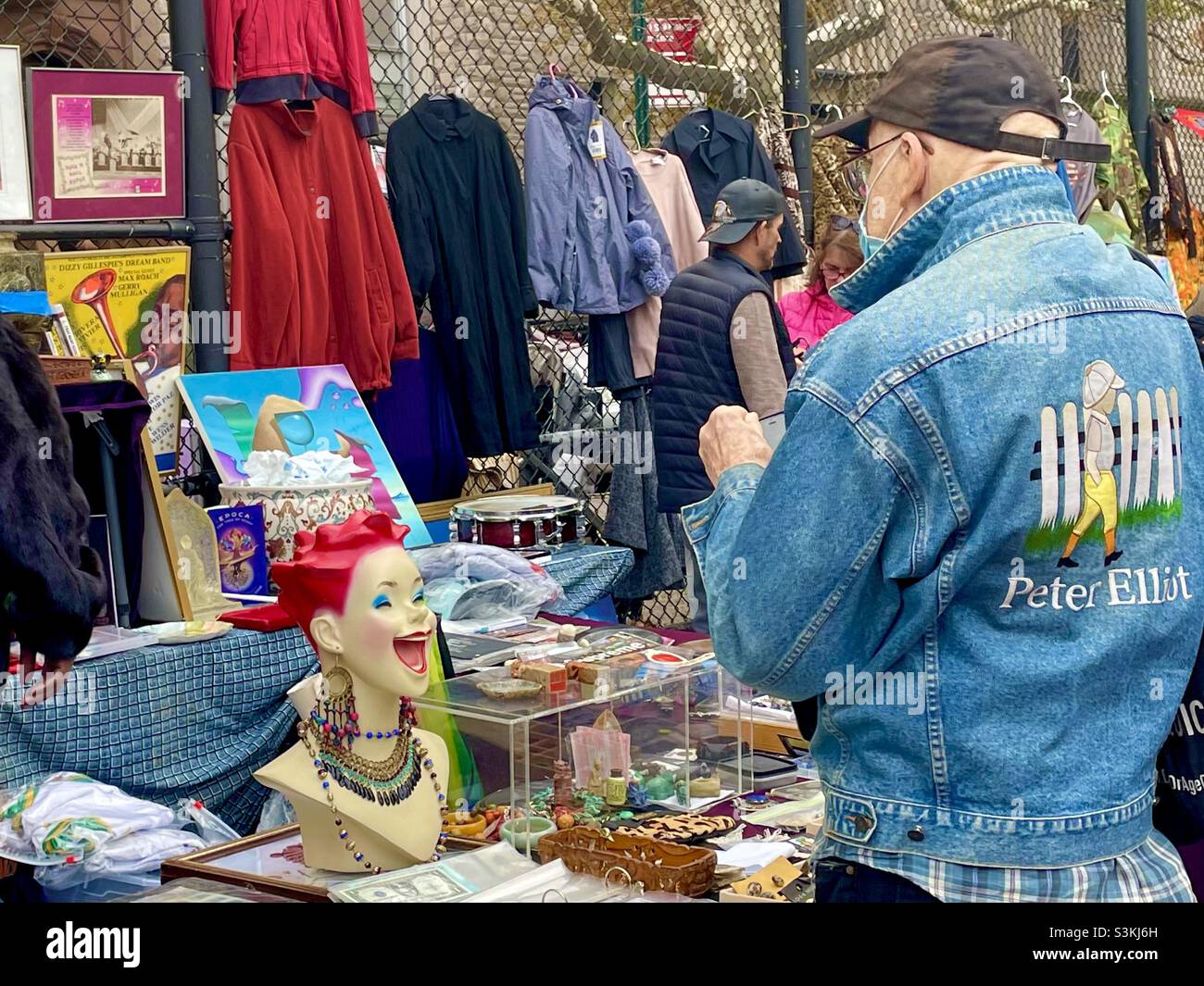 A man and a denim jacket shops at a vintage Booth at the grand bizarre in New York City - Smartphone Captured Stock Image