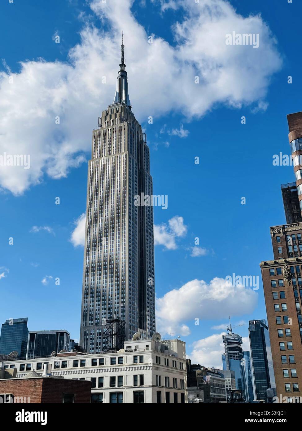 A view of the Empire State building looking toward Hudson yards from a high floor on a clear day with white fluffy clouds in New York City - Smartphone Captured Stock Image