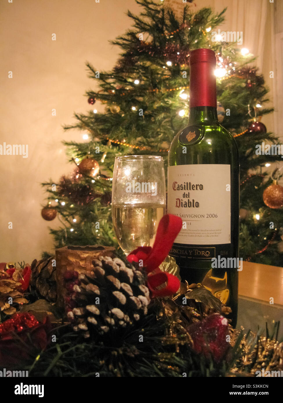 Christmas display of a decorated tree in the background, a bottle of wine and glass in the foreground with more Christmas decorations - Smartphone Captured Stock Image
