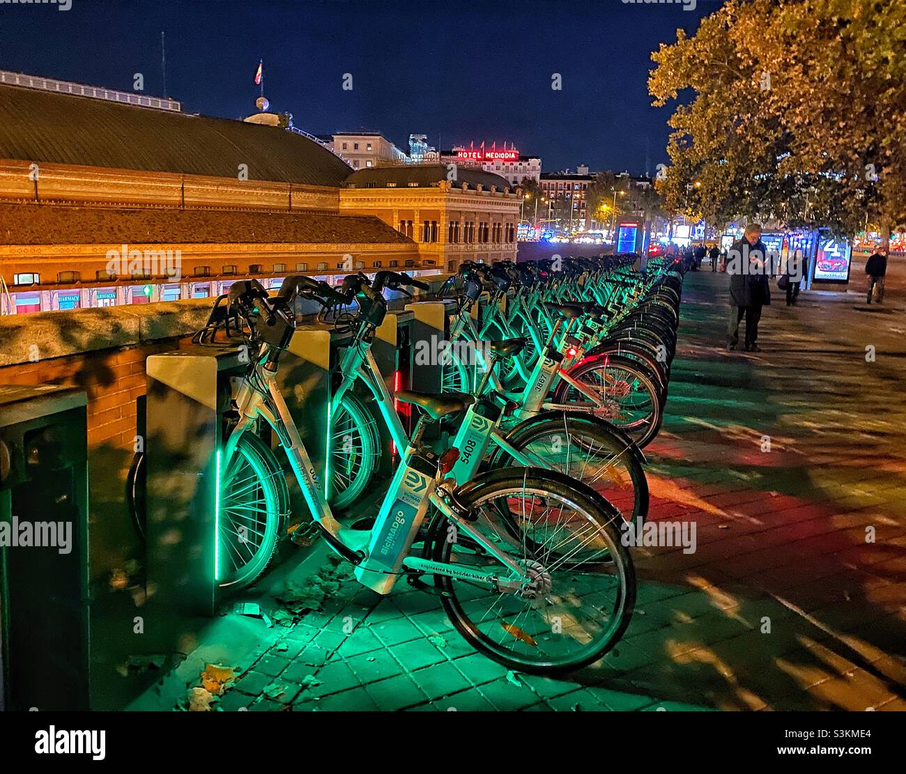 Electric bikes lined up for rental outside Atocha railway station in Madrid one evening after nightfall in autumn. The bikes are illuminated for the purposes of visibility and safety. Stock Photo