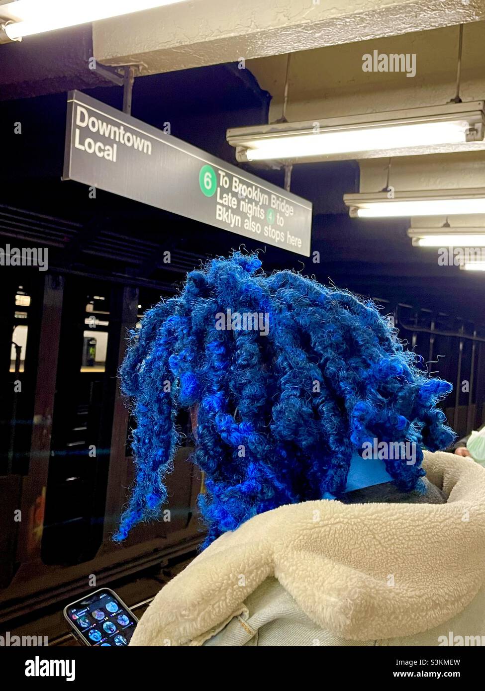A person with a blue Afro hairdo waits for the subway train in New York City - Smartphone Captured Stock Image