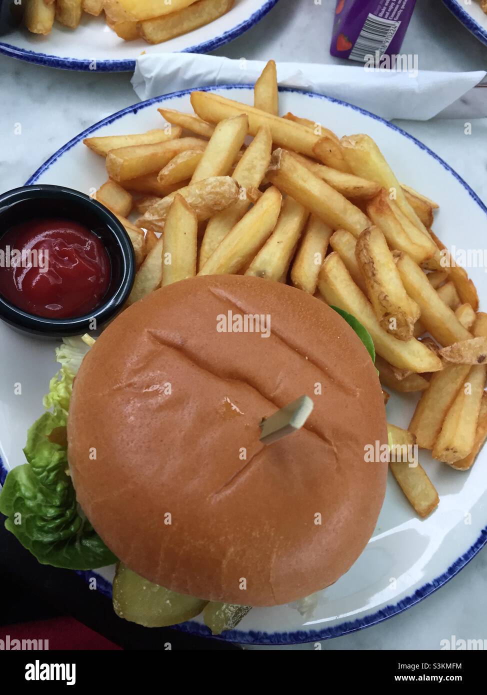 Vegan burger with gerkins. In a bun with chips on the side and a pot of ketchup Stock Photo