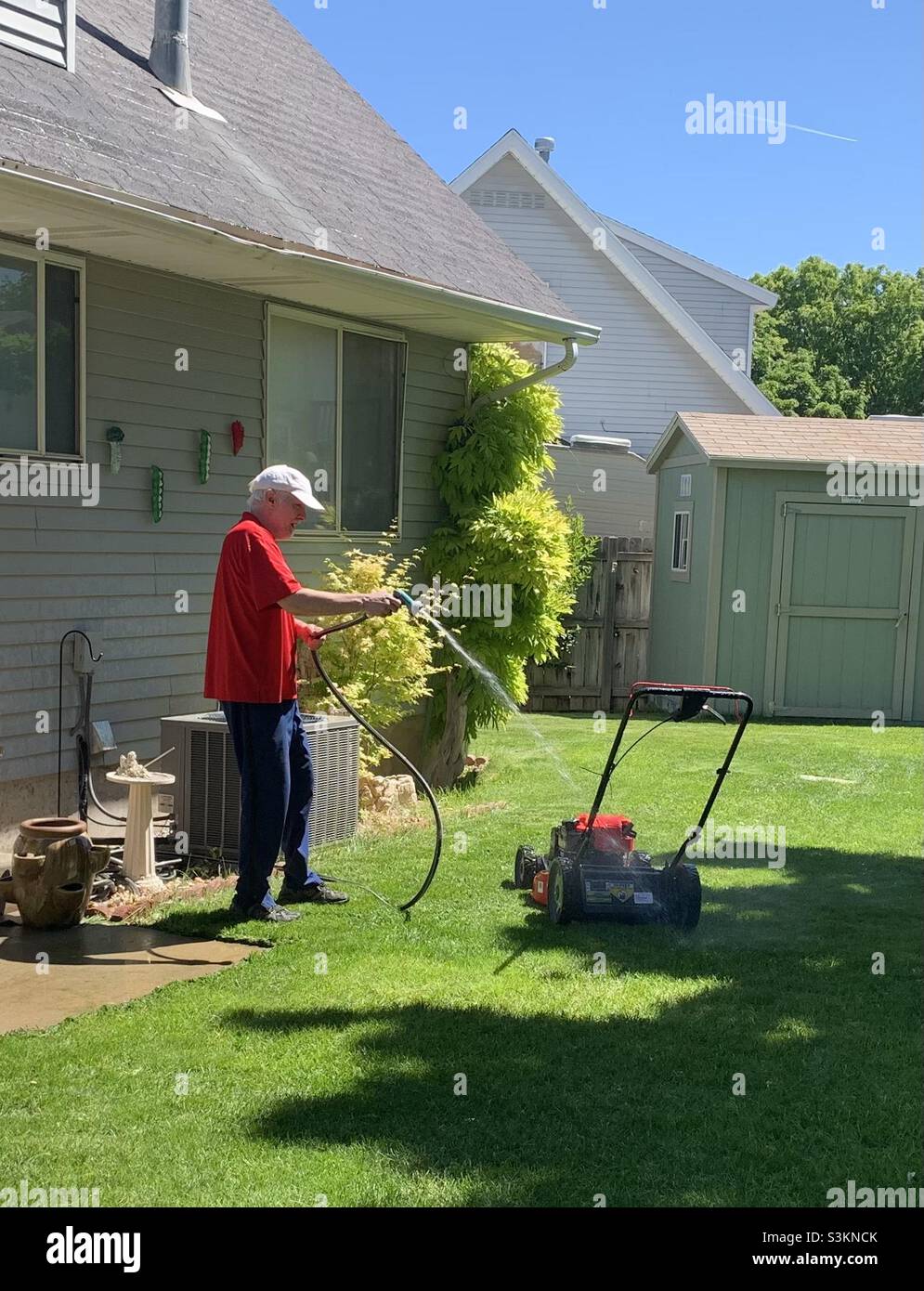 Man in his yard spraying off his mower as part of a spring cleanup in Utah, USA. - Smartphone Captured Stock Image