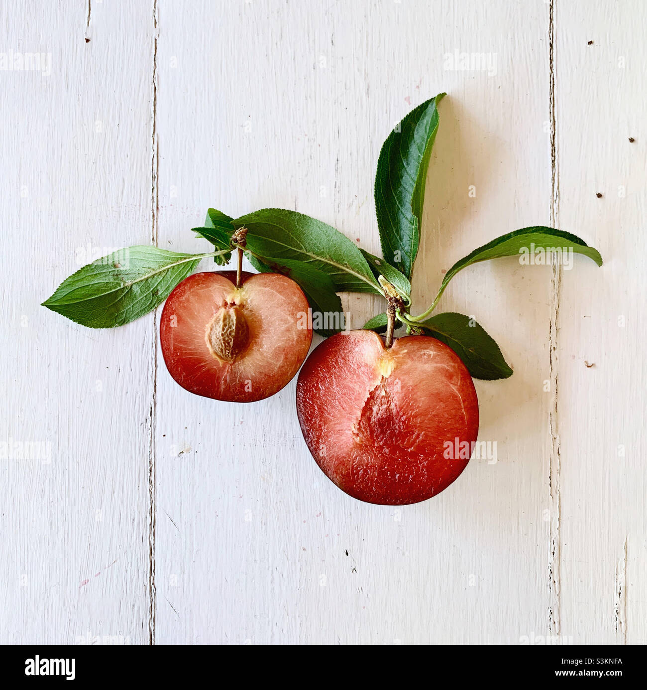 Open red plums on white wood Stock Photo