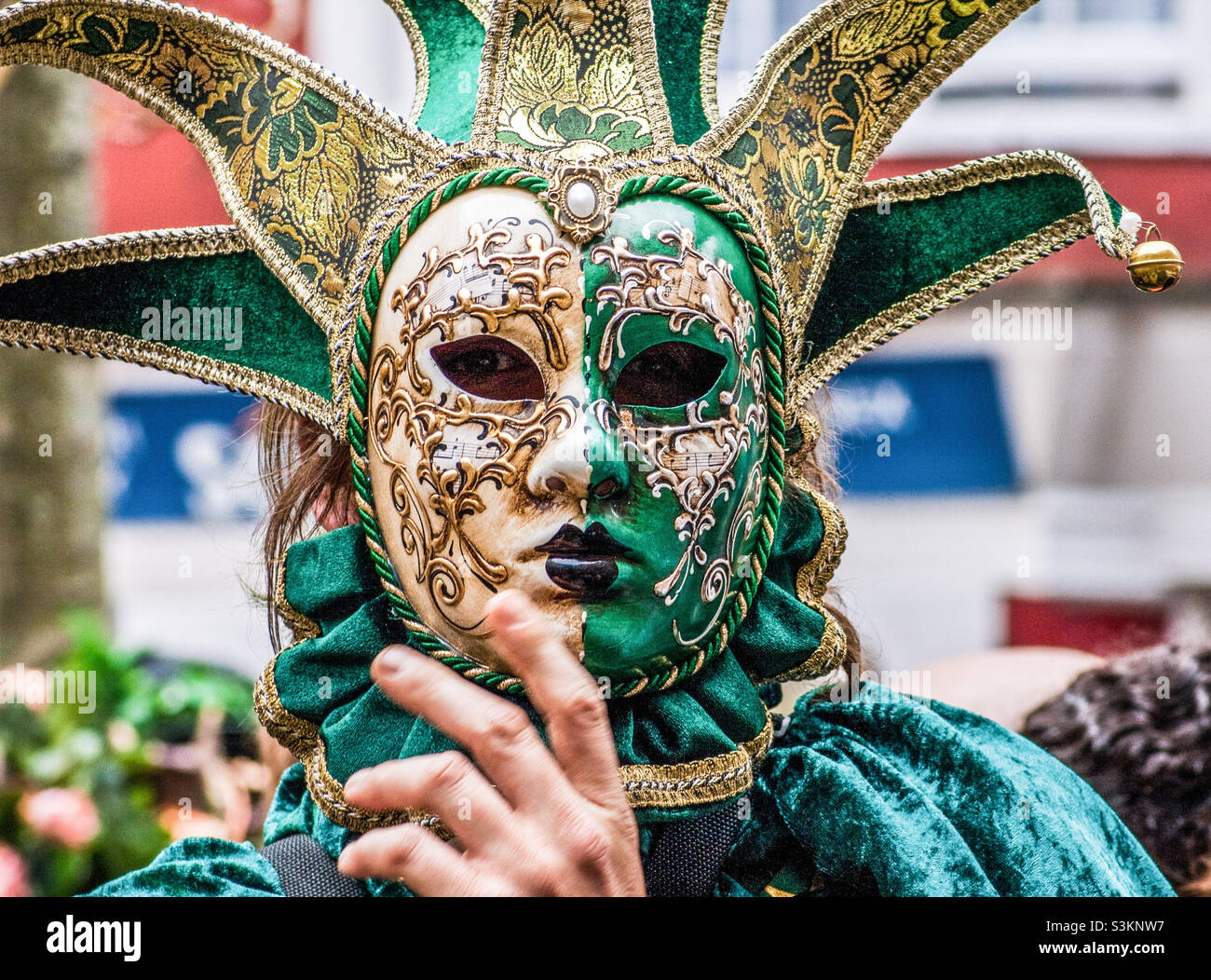 A reveller conceals their face behind an elaborate Venetian mask in green and gold - Smartphone Captured Stock Image