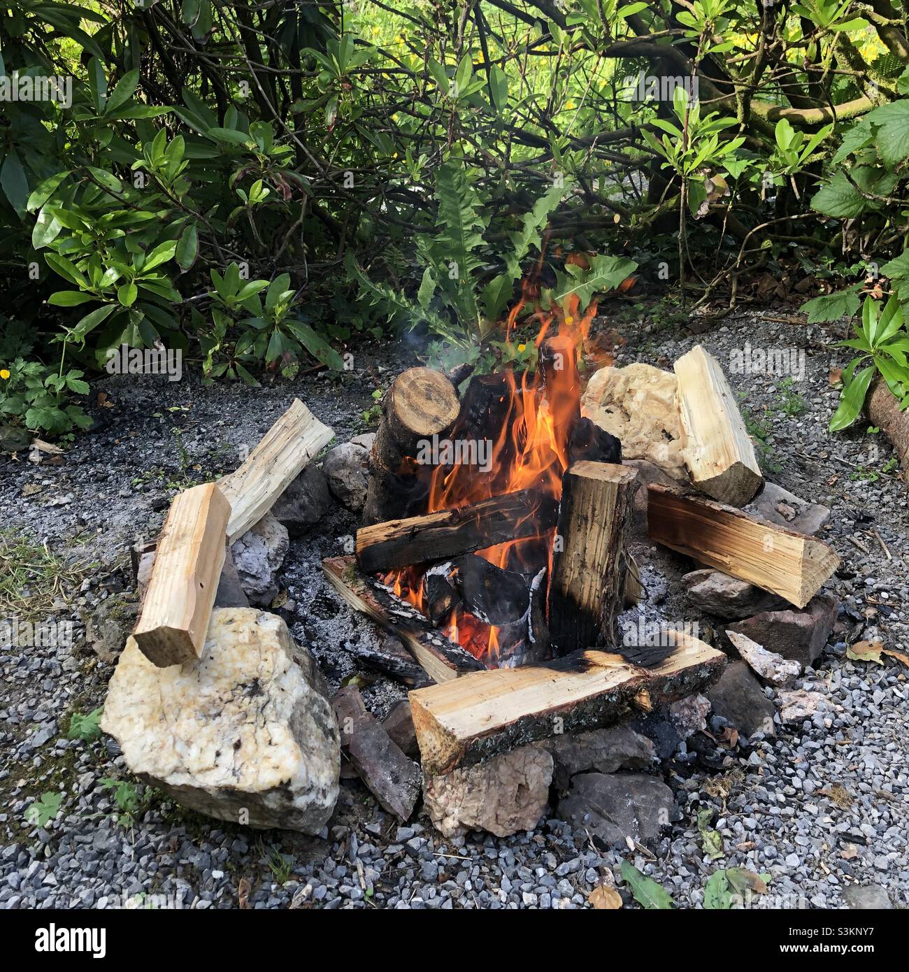 A campfire stacked with logs is burning on a gravel area - Smartphone Captured Stock Image