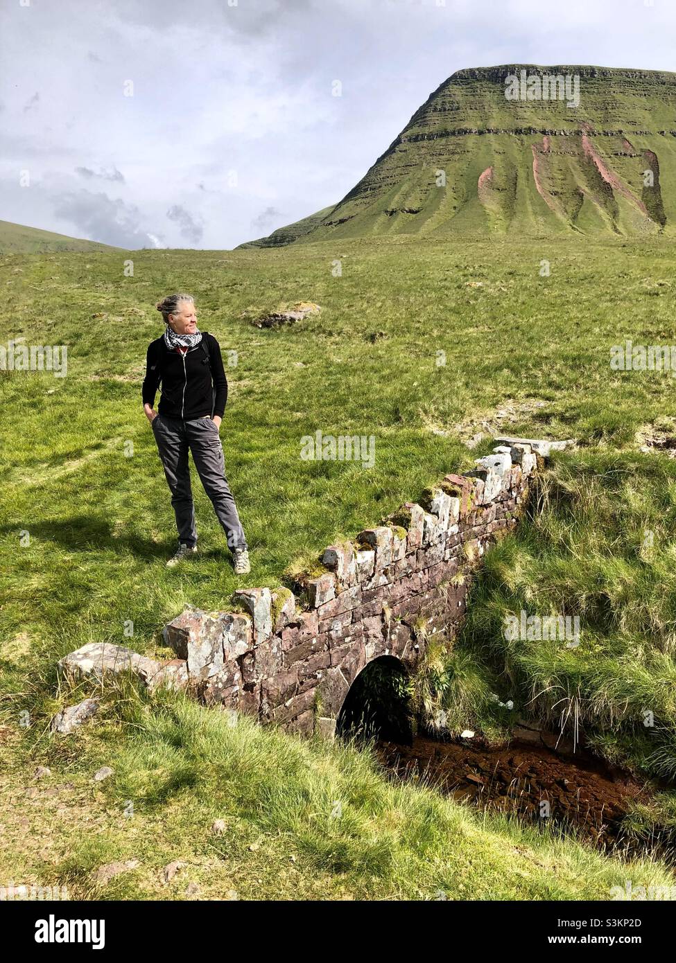A woman stands on an old bridge in the Brecon Beacon mountains in Wales - Smartphone Captured Stock Image