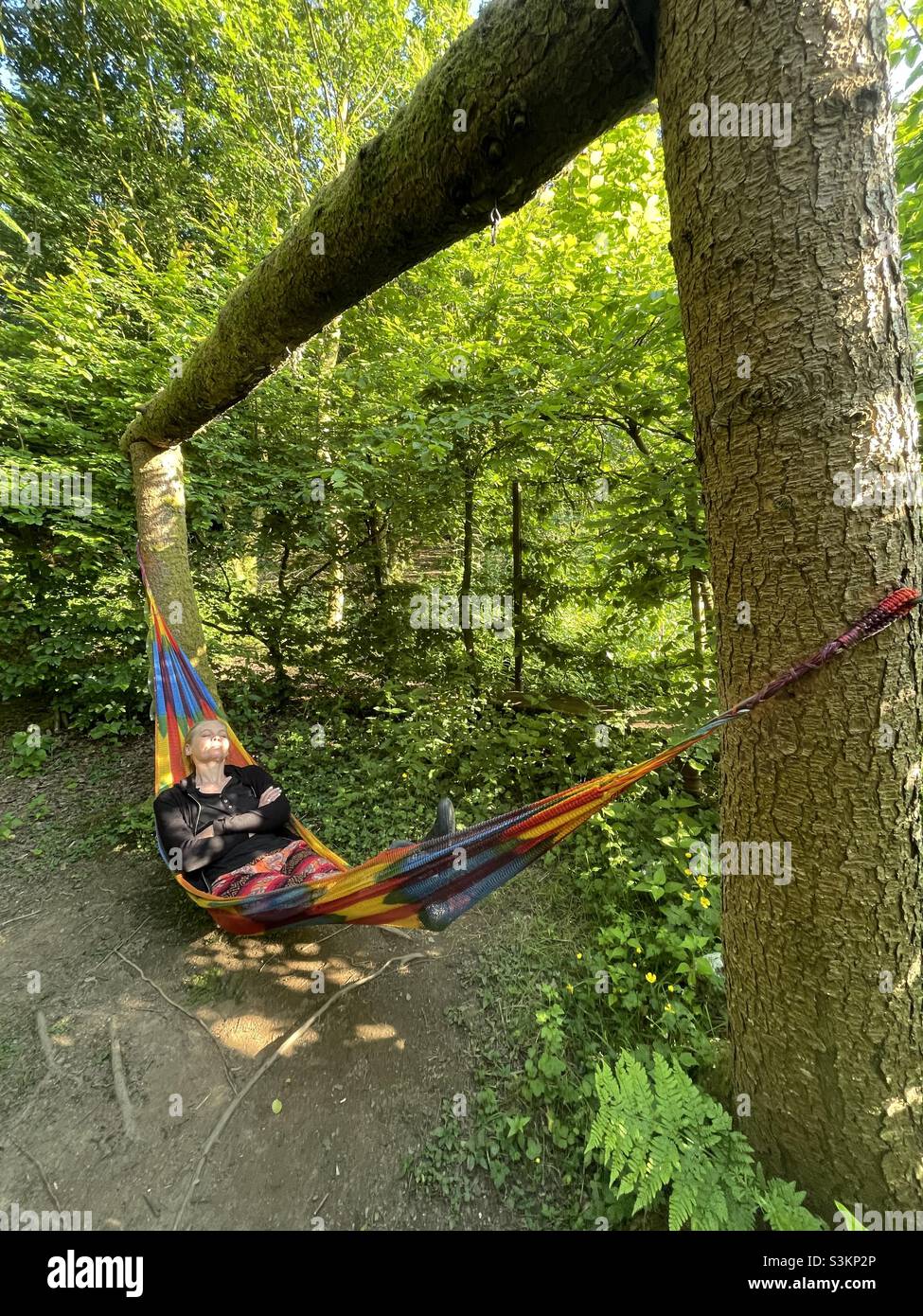 A woman swings in a colourful hammock in the woods in Wales - Smartphone Captured Stock Image