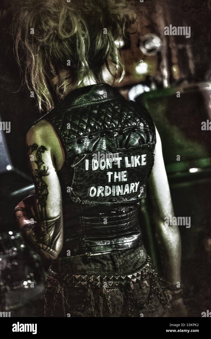 Blonde female musician stands with her back to the crowd, displaying the phrase “I don’t like the ordinary” on the back of her jacket - Smartphone Captured Stock Image