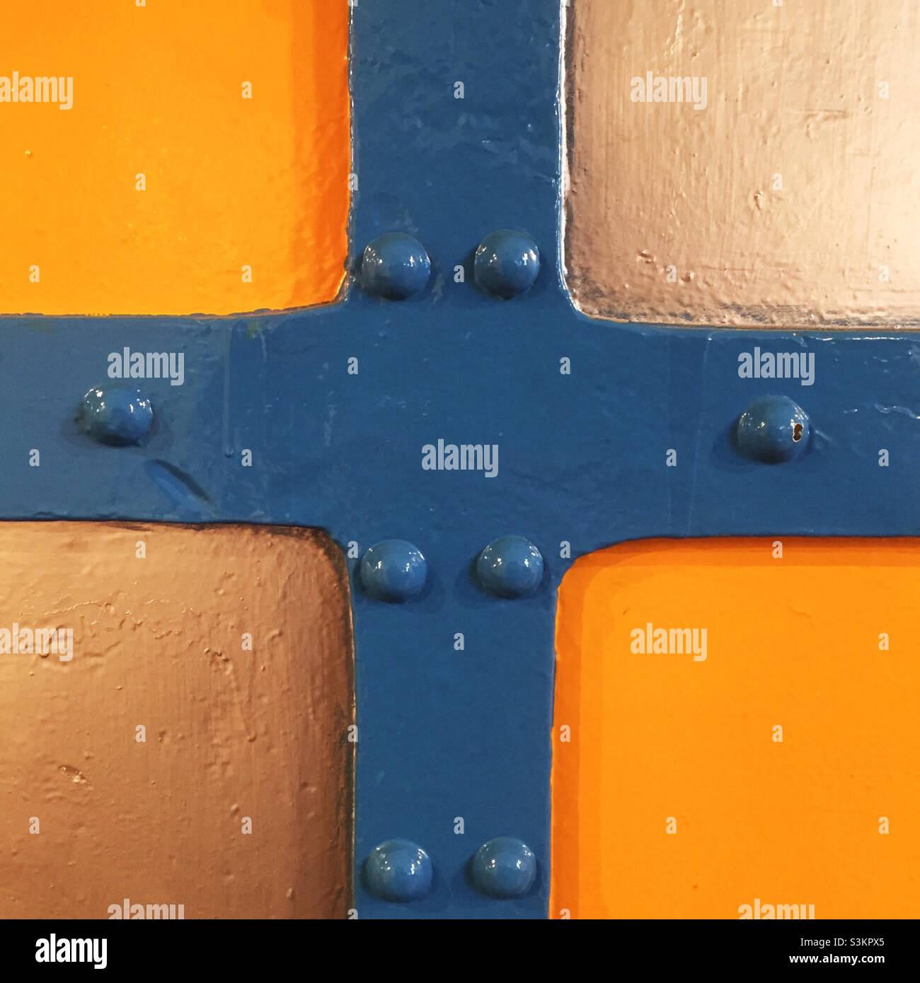 An abstract image of a metal, riveted door panel in blue, orange and white Stock Photo