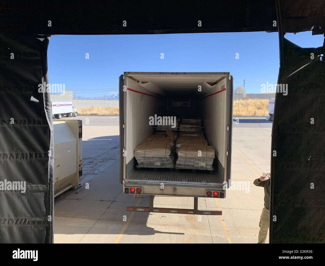 Semi truck loaded with pallets of paper products is seen backing up to a dock for unloading in