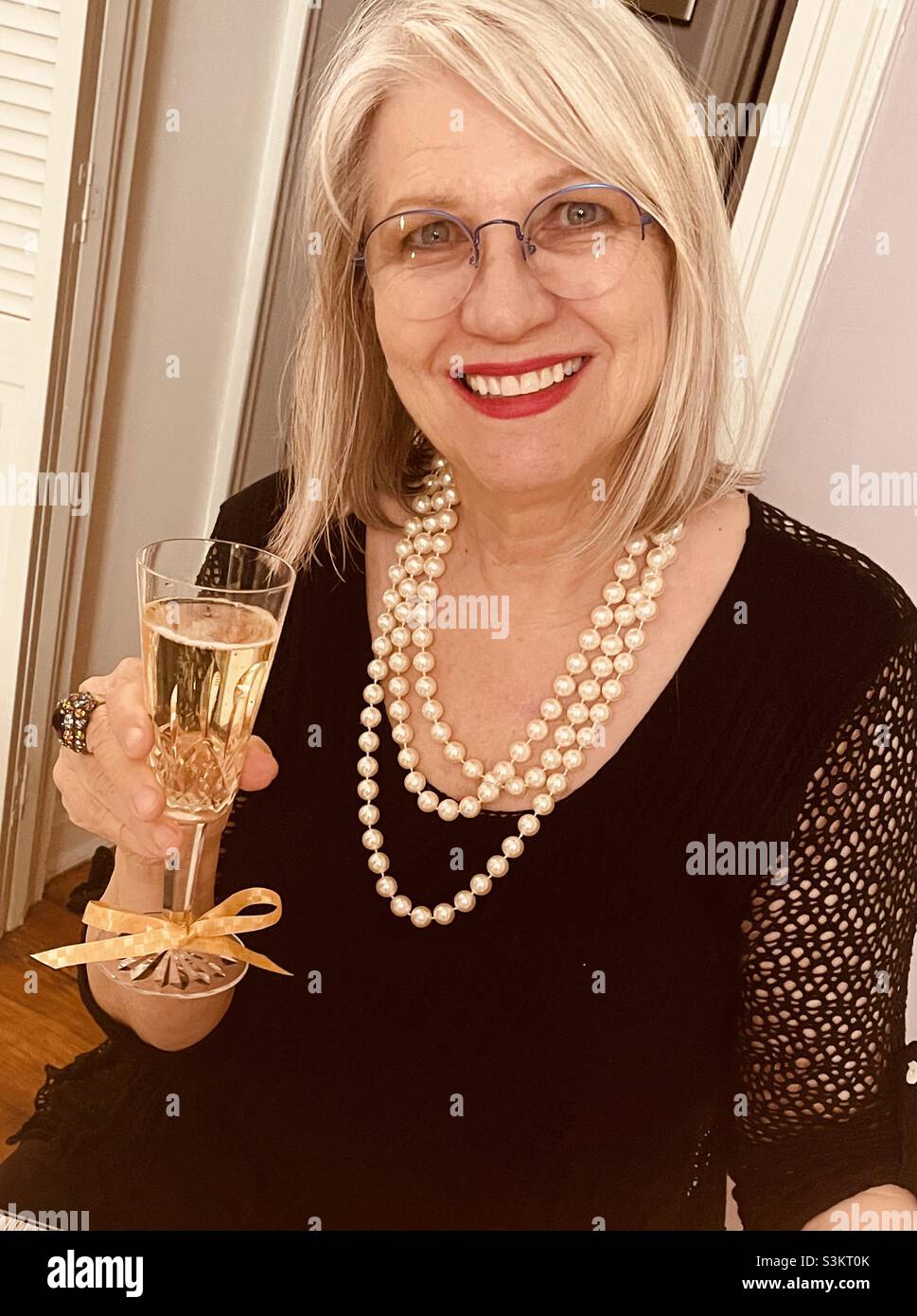 A blonde woman smiling with a flute of champagne - Smartphone Captured Stock Image