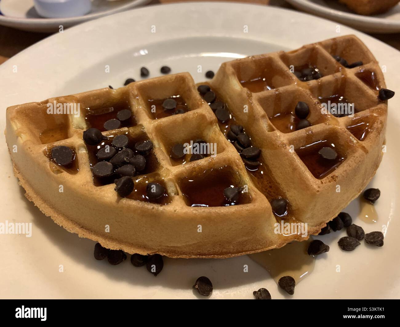 Half waffles with chocolate chips and syrup on a white round plate