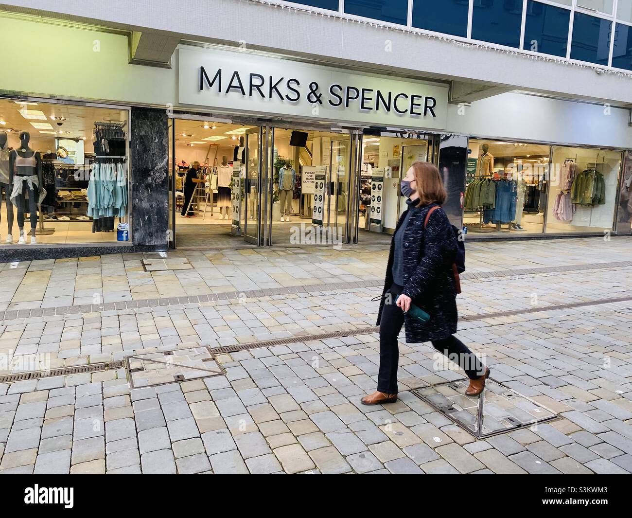 Woman walking past a branch of Marks and Spencer in Gibraltar - Smartphone Captured Stock Image