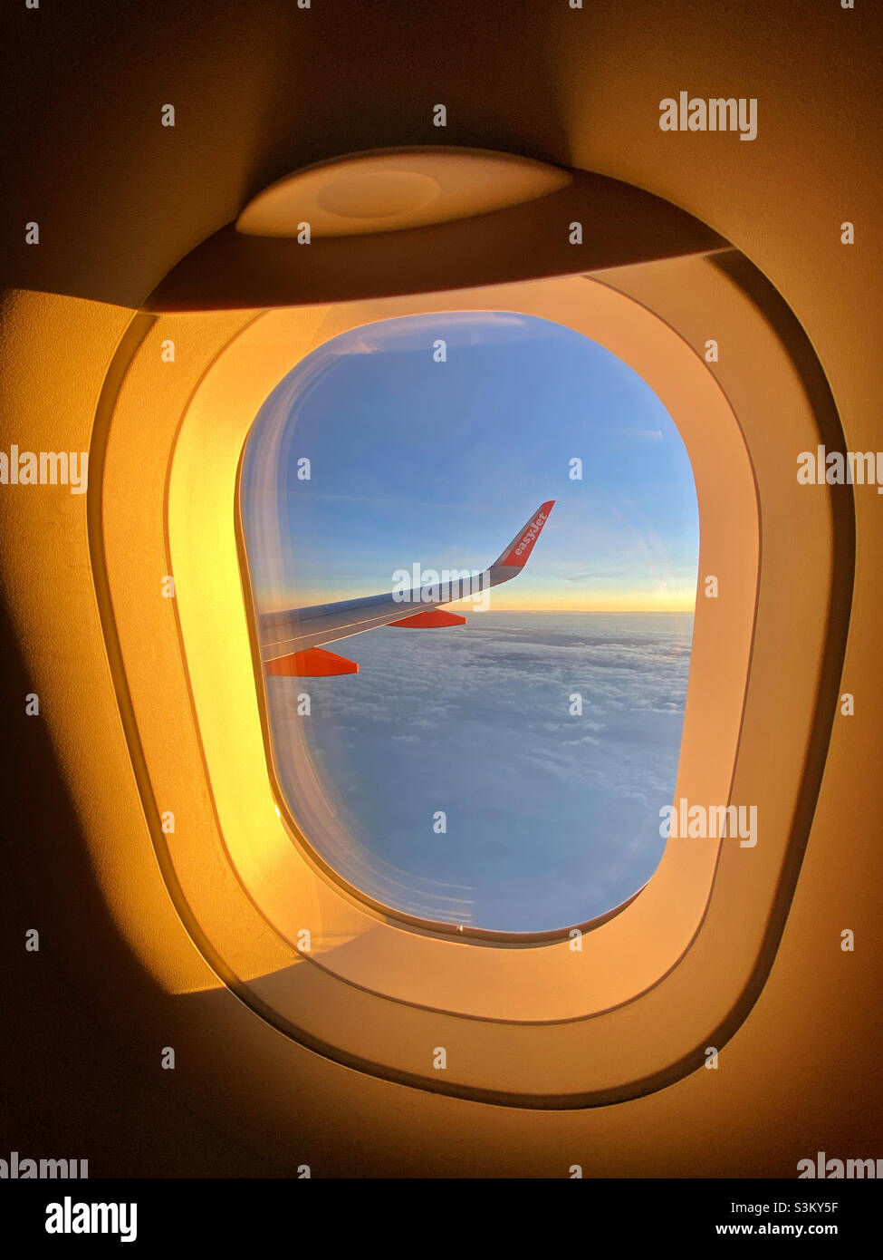 A view above the clouds - thousands of feet above the ground. A sunrise/sunset view of an EasyJet window and aircraft wing. Going on holiday or returning? Photo ©️ COLIN HOSKINS. - Smartphone Captured Stock Image