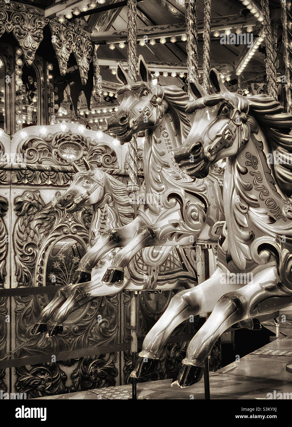 3 horses await new riders on a fairground carousel. A toned monochrome image evoking childhood memories from funfair merry go round rides. Photo ©️ COLIN HOSKINS. - Smartphone Captured Stock Image