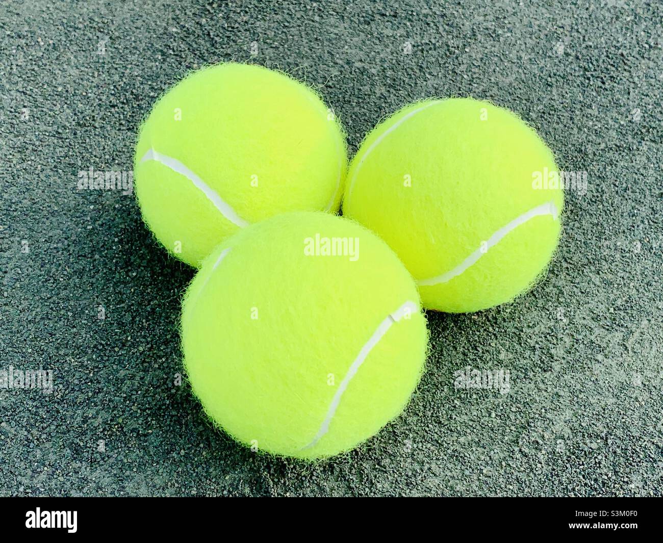 Three tennis balls on a gray clay courts. Stock Photo