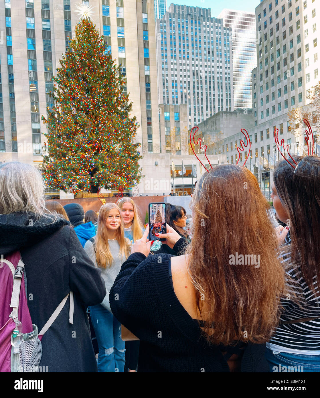 Attractive young ladies pose for photographs in front of the iconic Rockefeller Christmas tree during the holiday season in New York City 2021, United States - Smartphone Captured Stock Image