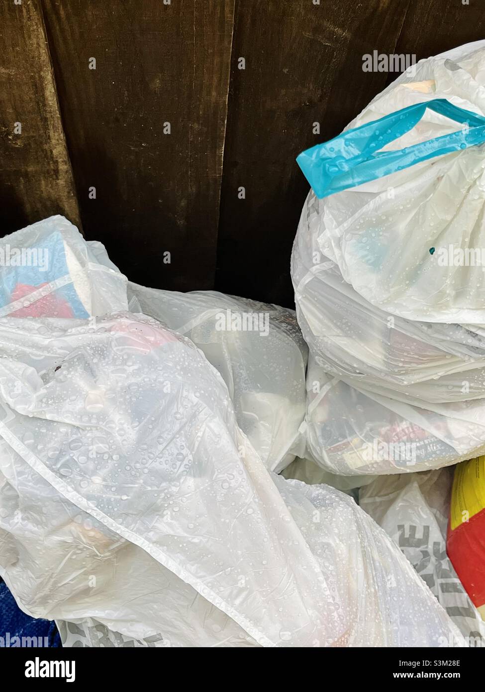 White bin bags with blue turquoise ties next to a rustic garden fence