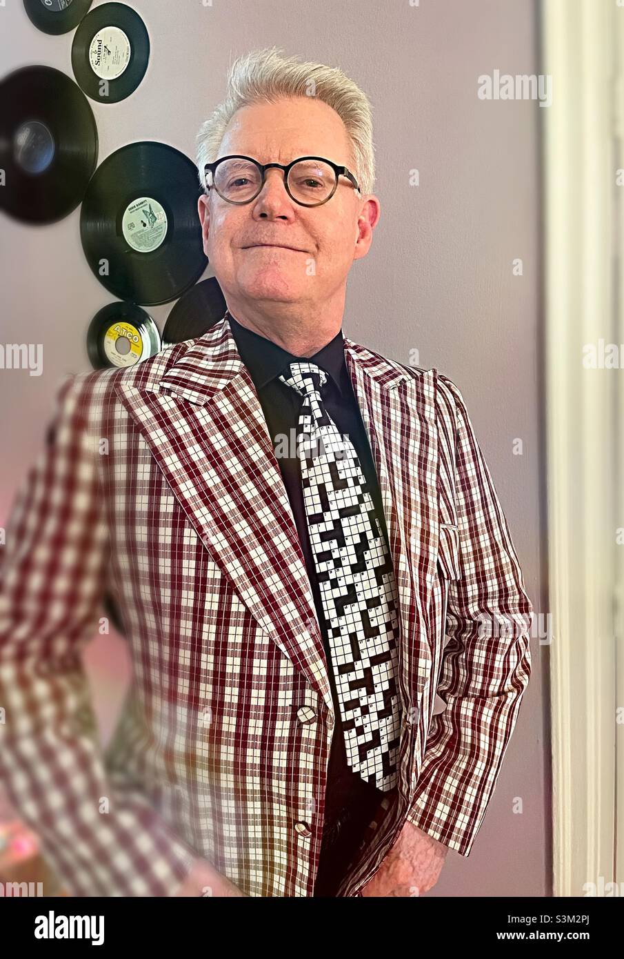 Senior man poses in a retro plaid jacket in front of vinyl records, 2021, New York City, United States - Smartphone Captured Stock Image