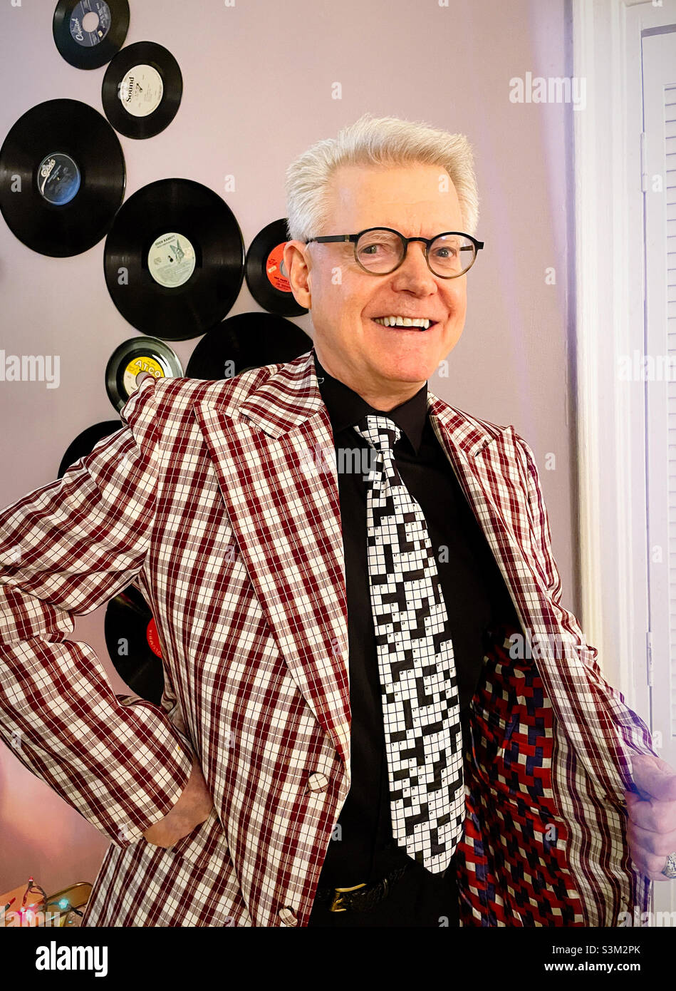 Senior man shows off his multi colored lining of a plaid jacket in front of a display of retro vinyl records, 2021, United States - Smartphone Captured Stock Image