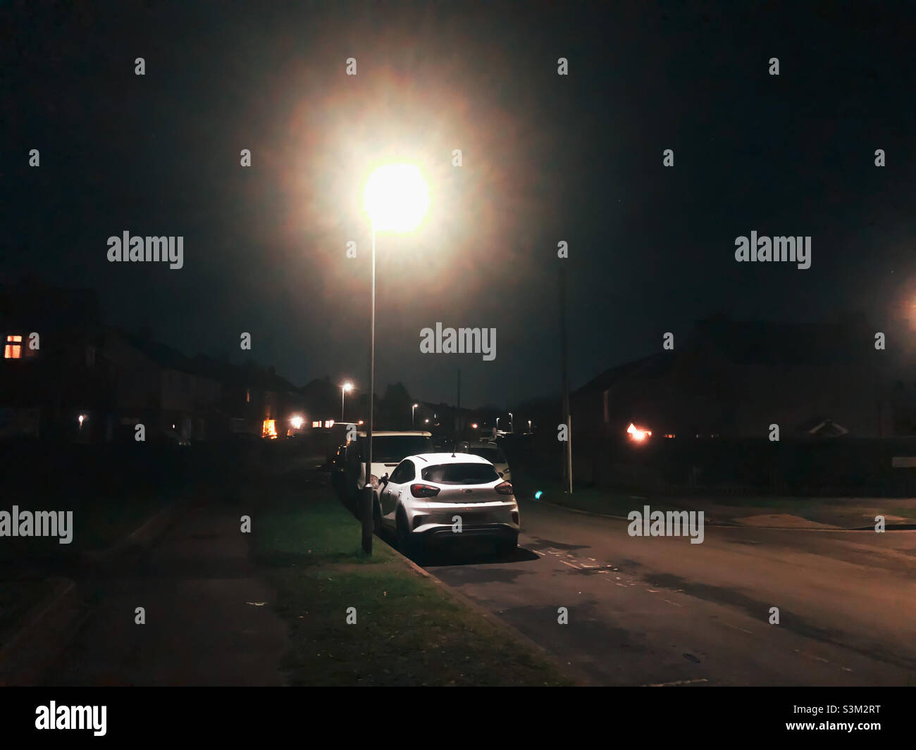 Cars parked under a lamppost on a dark night in a suburban street. - Smartphone Captured Stock Image