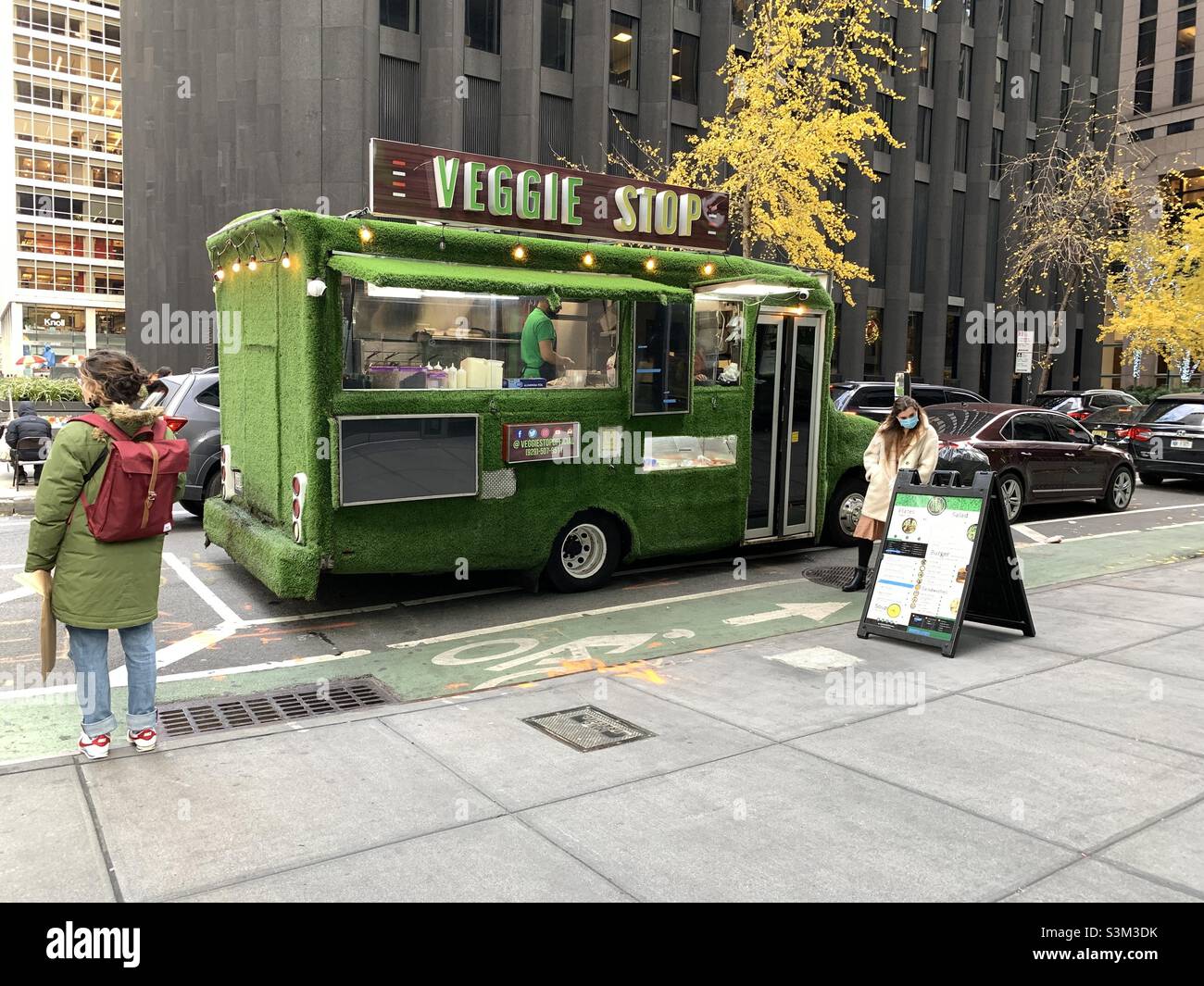 One woman standing looking out on the other side. Another woman standing looking the menu at veggie stop. - Smartphone Captured Stock Image