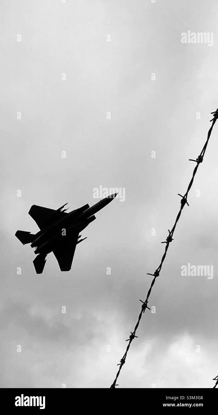 Jet over Barb. Silhouette of training fighter jet flying over barbed wire viewpoint security fence at RAF Lakenheath, Suffolk. Stock Photo