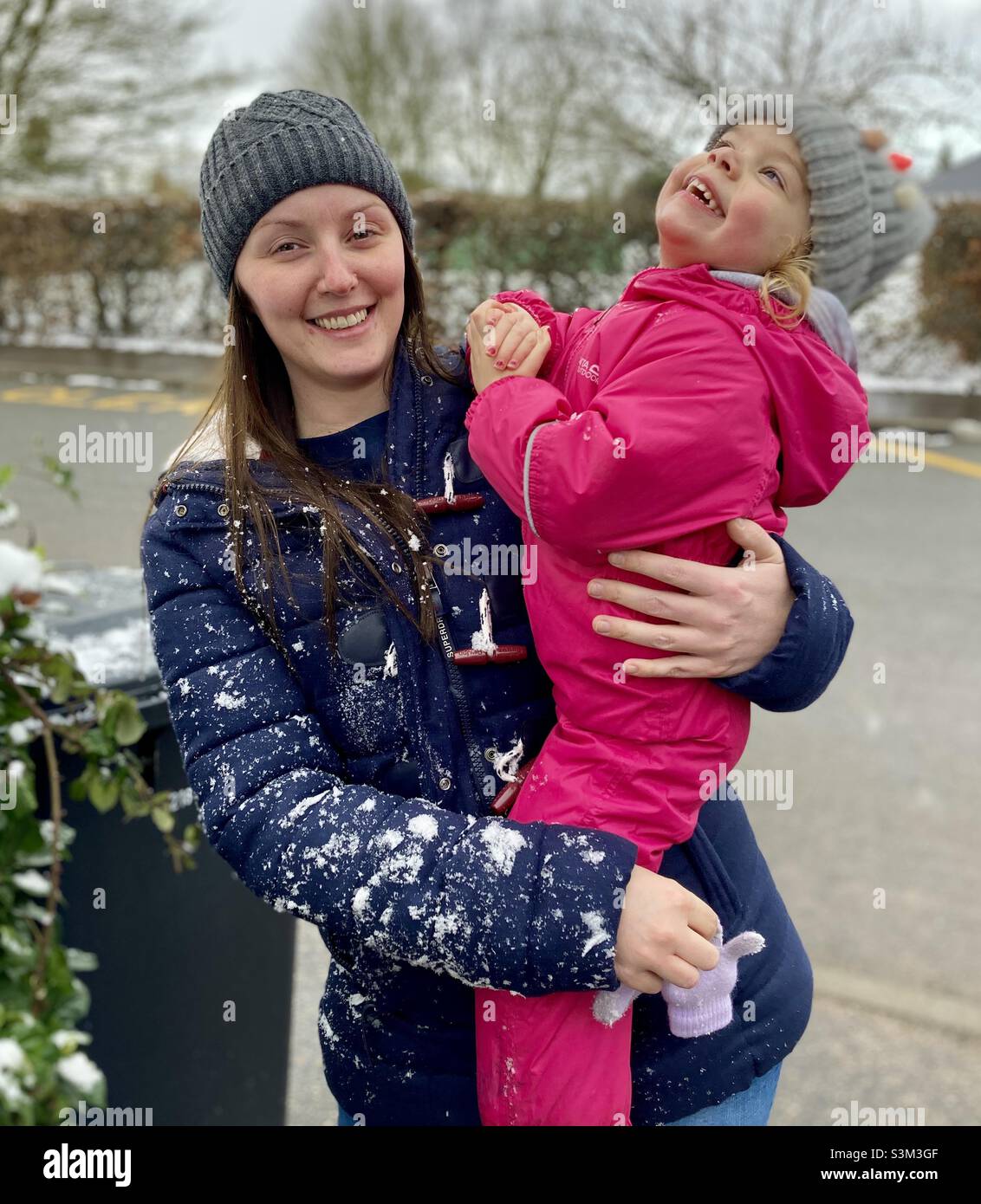 Winter Fun. Happy image of young, smiling woman holding a rosy cheeked toddler. Both wearing warm, outdoor clothing. Snow evident. Stock Photo