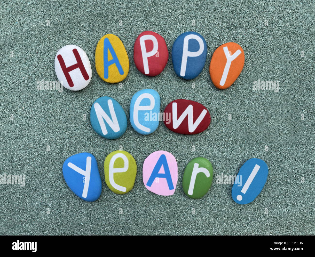 Happy New Year, creative text composed with hand painted multi colored stone letters over green sand Stock Photo