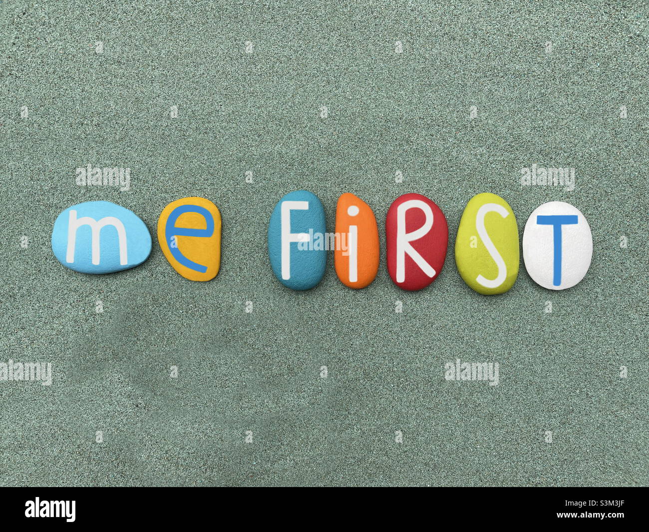 Me first, motivational slogan composed with multi colored stone letters over green sand - Smartphone Captured Stock Image