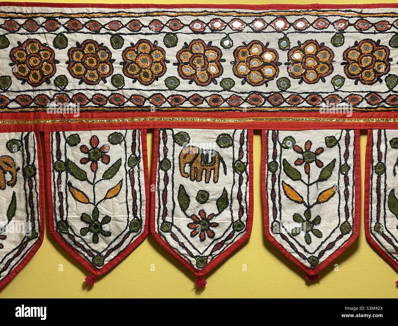 An Indian embroidery in traditional style with mirror work such as might be hung over a door. Motifs include elephants and flowers - Smartphone Captured Stock Image