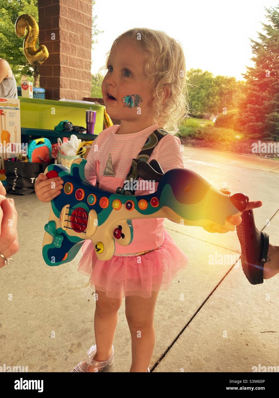 Two year old blonde girl with guitar toy present at her birthday party. - Smartphone Captured Stock Image