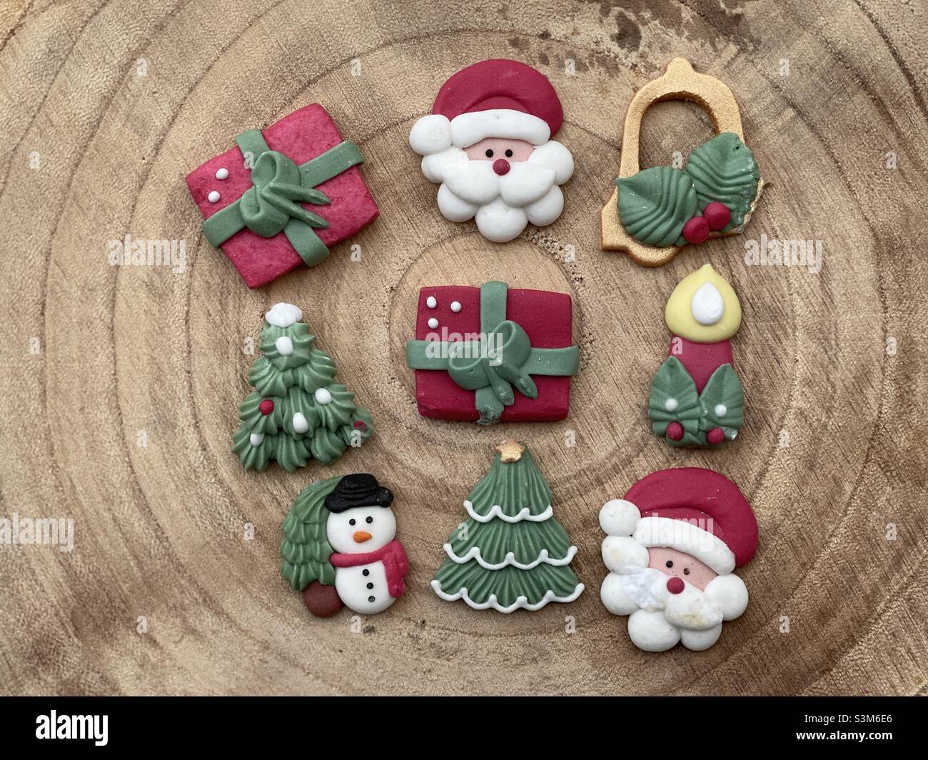 Christmas marzipan ornaments on a wooden board with a candle, snowman, santa claus, christmas tree, presents and christmas bell Stock Photo